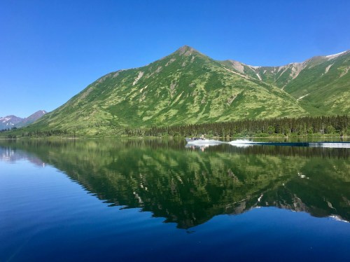 A serene lake reflecting a lush green mountain under a clear blue sky.