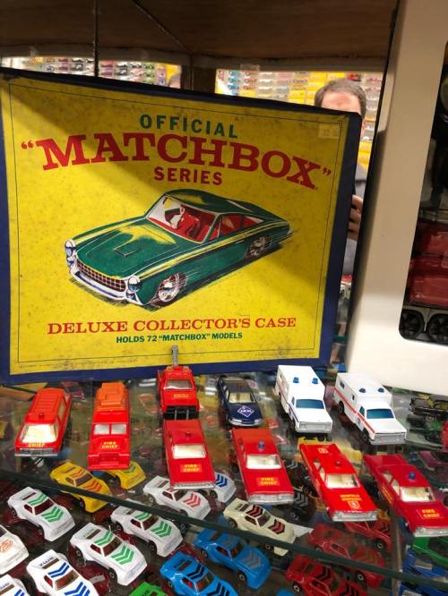 A vintage Matchbox collector's case with a classic car design, surrounded by various toy cars displayed underneath.