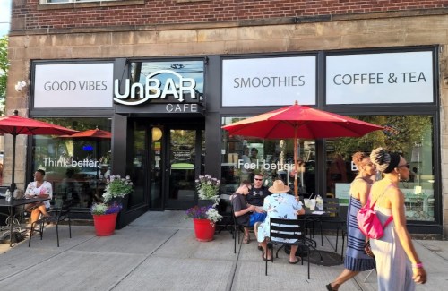 Exterior of UnBAR Cafe with outdoor seating, umbrellas, and people enjoying smoothies and coffee. Bright and inviting atmosphere.