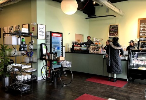 A cozy café interior with a counter, barista, customers, and a display of pastries and drinks.