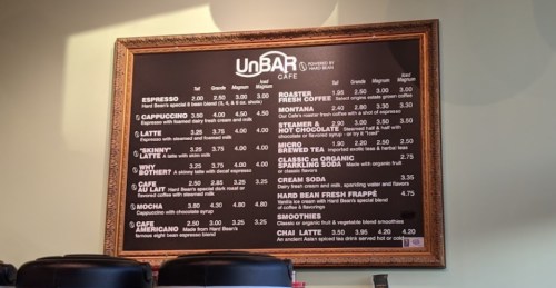 Menu board at UnBAR Café featuring coffee drinks, prices, and specialty items in a framed display.