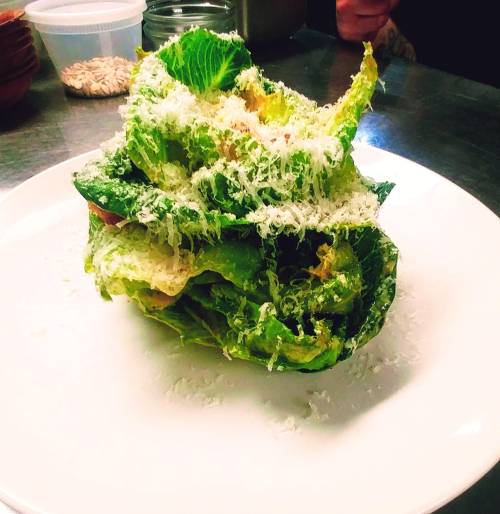 A plate with a tall stack of romaine lettuce topped with grated cheese, set in a kitchen environment.