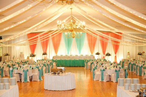 Elegant banquet hall decorated with teal and coral drapes, tables set with white linens and teal chair sashes.
