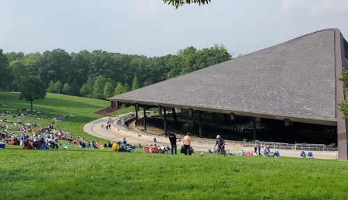 A large outdoor amphitheater surrounded by a grassy area filled with people enjoying a sunny day.