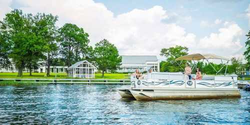 A pontoon boat with people on a lake, surrounded by trees and a building in the background under a cloudy sky.