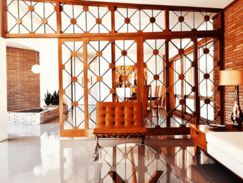 A modern interior featuring a wooden partition with geometric patterns, a brown sofa, and sleek furniture.