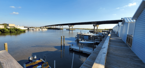 A serene waterfront scene with boats docked along a wooden pier and a bridge spanning the water in the background.