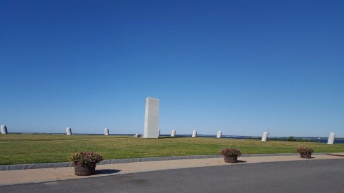 A clear blue sky over a grassy area with several stone monuments and flower planters along a pathway.