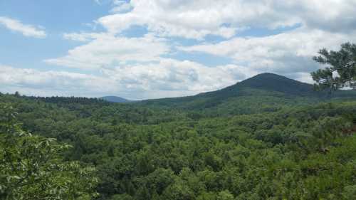 A panoramic view of lush green mountains and valleys under a partly cloudy sky.