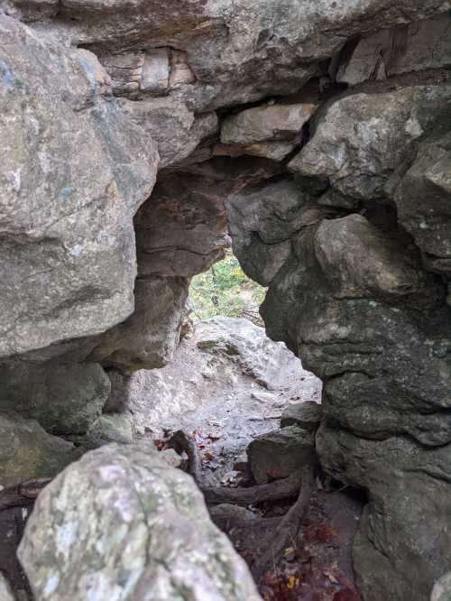 A narrow passageway between large rocks, leading to a view of greenery beyond.