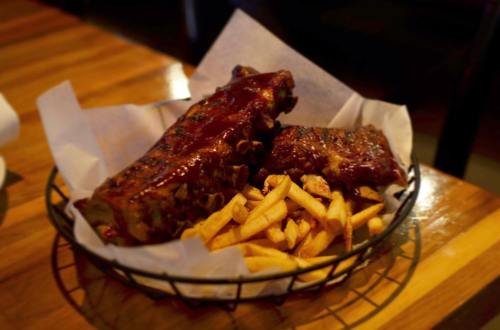 A basket of barbecue ribs with a side of golden fries, served on a wooden table.