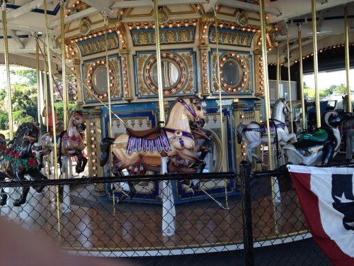 A colorful carousel with ornate horses, featuring gold accents and decorative details, surrounded by a fence.