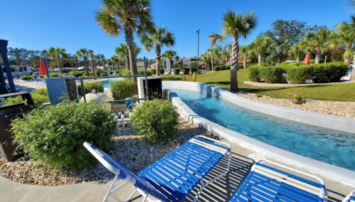 A sunny pool area with a lazy river, lounge chairs, and palm trees in a landscaped setting.