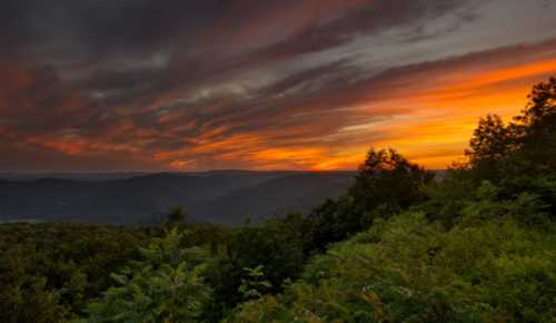 A vibrant sunset over rolling hills, with dramatic clouds and lush greenery in the foreground.