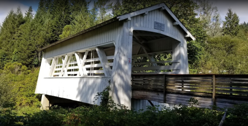 A white wooden covered bridge surrounded by lush greenery and trees.