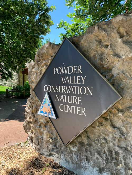 Sign for Powder Valley Conservation Nature Center, mounted on a stone wall, surrounded by greenery.