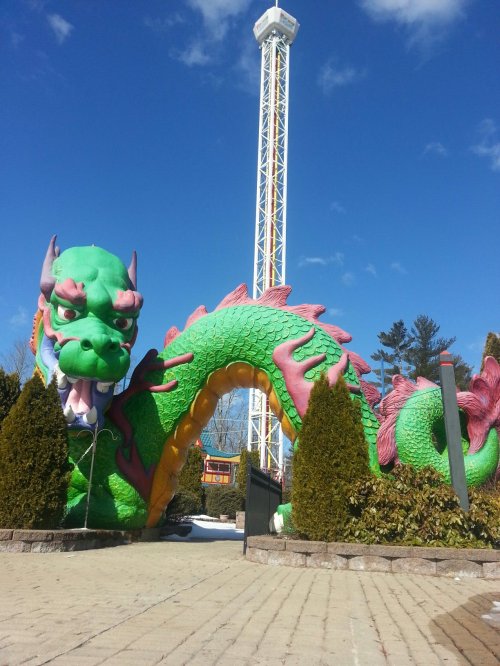 A large green and pink dragon sculpture with a tower ride in the background against a blue sky.