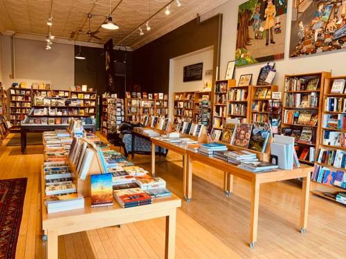 A cozy bookstore interior with wooden tables displaying books and shelves filled with various titles in the background.
