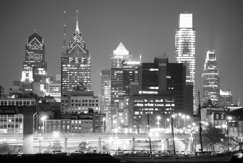 Black and white cityscape of Philadelphia at night, featuring illuminated skyscrapers and a bridge.