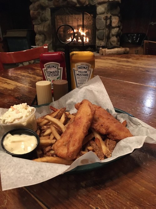 A plate of golden fried fish and fries, served with coleslaw and dipping sauces, set on a rustic wooden table.