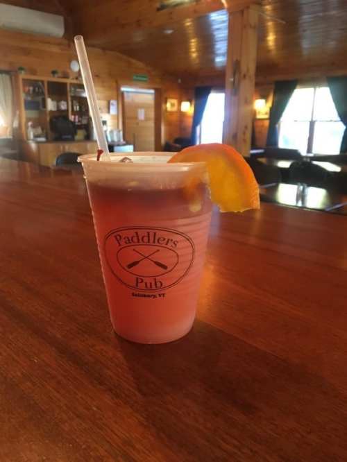 A drink with a slice of orange sits on a wooden bar in Paddlers Pub, with a cozy interior in the background.