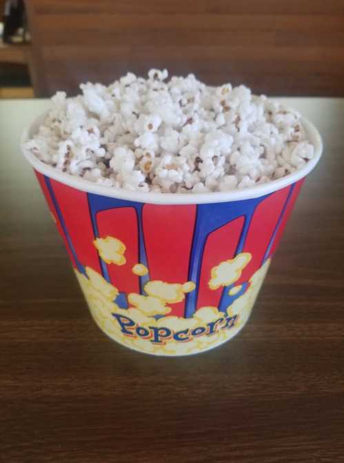 A colorful popcorn bucket filled with fluffy popcorn, sitting on a wooden table.