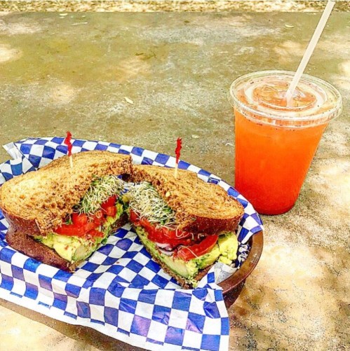 A sandwich with tomatoes and sprouts on whole grain bread, served with a refreshing orange drink in a clear cup.