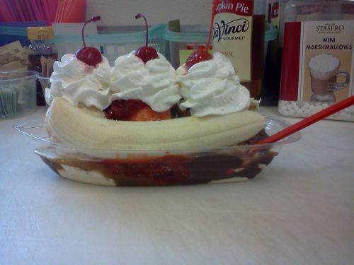 A banana split topped with whipped cream and cherries, served in a clear dish with chocolate and strawberry sauce.