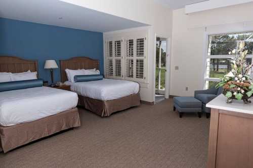 A spacious hotel room with two beds, a seating area, and large windows letting in natural light.