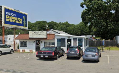 A small restaurant with a sign, surrounded by parked cars and a large billboard in the background.