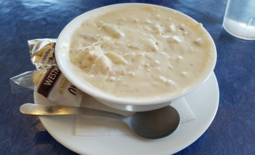 A bowl of creamy soup with chunks, served with a spoon and a pack of crackers on a plate.