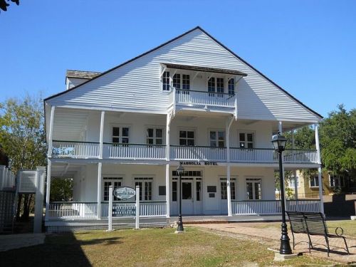 A white, three-story hotel with a porch and balconies, set against a clear blue sky.