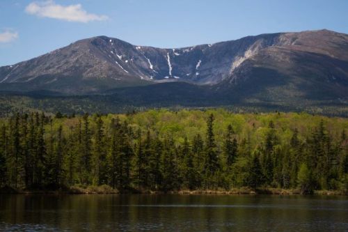 A serene landscape featuring a mountain with snow-capped peaks, lush green trees, and a calm lake in the foreground.