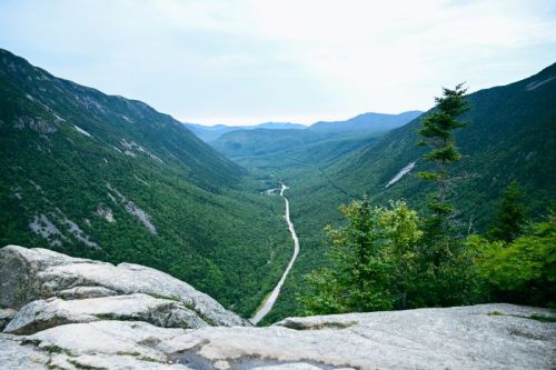 A scenic view of a lush green valley surrounded by mountains, with a winding road cutting through the landscape.