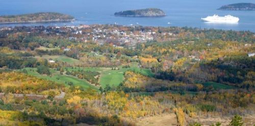 A scenic view of a coastal town surrounded by colorful autumn foliage and a cruise ship in the distance.