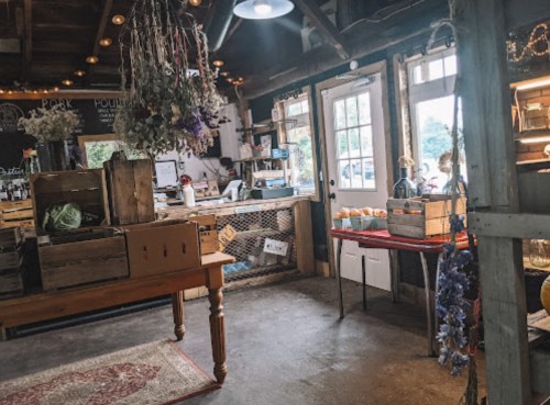 A rustic shop interior with wooden crates, a table, and dried flowers, featuring a bright entrance and cozy atmosphere.