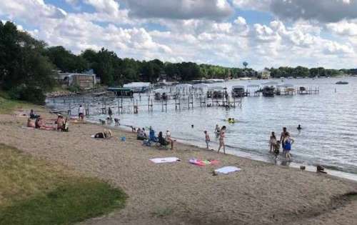 A sandy beach with people enjoying the water, boats in the distance, and a cloudy sky overhead.