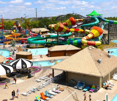 A vibrant water park featuring colorful slides, pools, and cabanas under a sunny sky. Families enjoy the attractions.