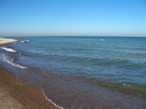 A calm beach scene with gentle waves lapping at the shore under a clear blue sky.