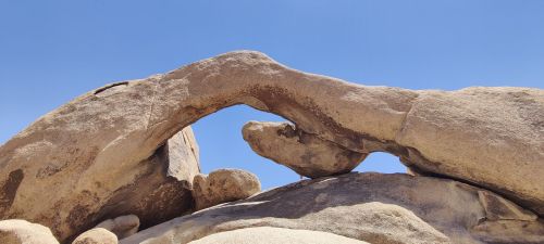 A natural rock formation resembling an arch against a clear blue sky.