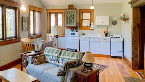 Cozy living space with a sofa, wooden furniture, and a small kitchen area featuring a stove and refrigerator.