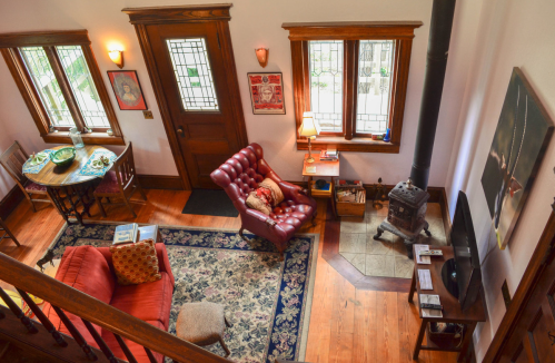 Cozy living room with a red armchair, wooden furniture, a small stove, and large windows letting in natural light.