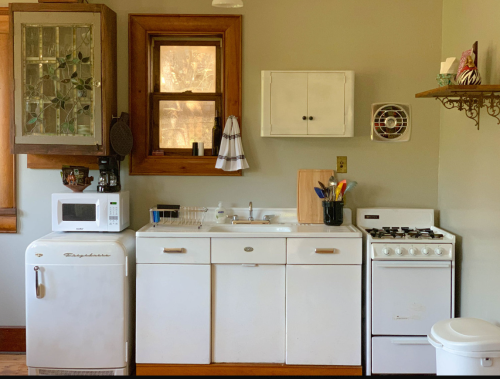 A cozy kitchen featuring a white sink, stove, refrigerator, and microwave, with wooden accents and a window.