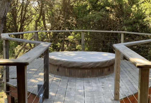 A circular wooden platform surrounded by trees, featuring a cushioned seating area and a railing.
