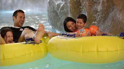 A family enjoys a fun day at a water park, floating on yellow inner tubes and smiling together.