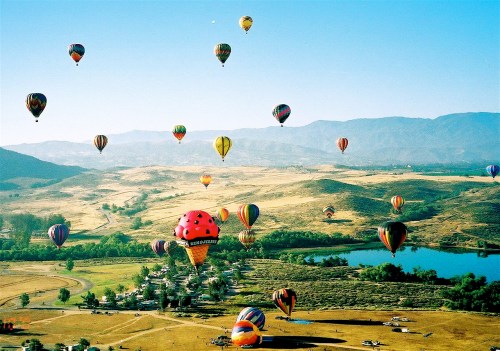 A vibrant sky filled with colorful hot air balloons over a scenic landscape with hills and a lake.
