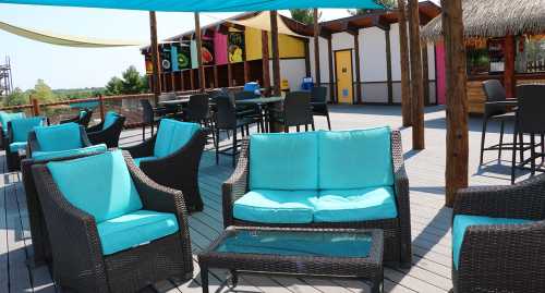 Outdoor seating area with turquoise cushions, wooden deck, and colorful decor in the background.