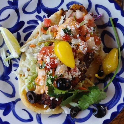 A colorful taco topped with grilled fish, fresh salsa, cheese, and garnished with lime and peppers on a decorative plate.