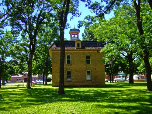 A historic brick building surrounded by lush green trees and grass on a sunny day.