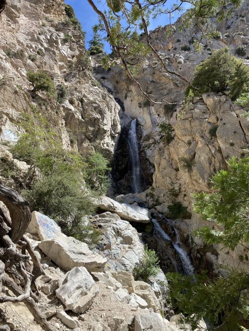A scenic waterfall cascading down rocky cliffs, surrounded by lush greenery and rugged terrain.
